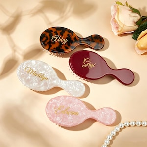 May include: Four oval hair brushes with short handles, each featuring a unique finish: one tortoise shell, one solid deep red, one white marbled, and one pink marbled. Each brush is personalized with gold cursive text reading Abby, Gigi, Madelyn, and Edwina.