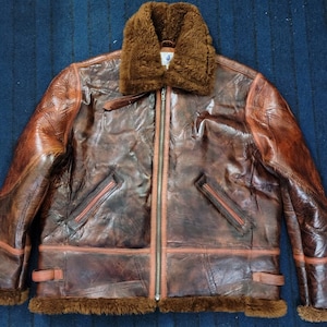 May include: A brown leather bomber jacket with a shearling collar and brown fur lining. The jacket has a zip closure and multiple pockets.
