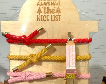 May include: Wooden display with the text "Teachers Always Make the Nice List" and three colourful hair ties: red, yellow, and pink. A pencil-shaped hair clip is also included. The words "DIGITAL FILE ONLY" are at the top.