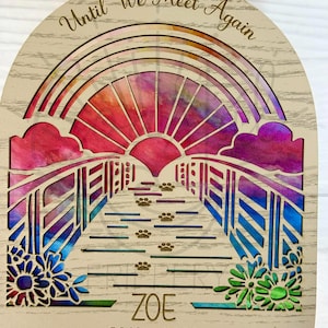 May include: Wooden memorial ornament with a rainbow bridge design. Features a rainbow, paw prints, and the text "Until We Meet Again." Includes the name "Zoe" and dates "2010-2023." Decorative flowers are on the bottom corners. The text "DIGITAL FILE ONLY" is at the top.
