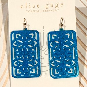 May include: A pair of blue glitter earrings with a geometric design. The earrings are rectangular in shape and have a delicate, intricate pattern. The earrings are labeled "Elise Gage Coastal Frippery" and "Digital File Only".