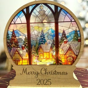 May include: A wooden Christmas decoration with a stained-glass window design. The scene depicts a snowy village with illuminated houses and trees. The text "Merry Christmas 2025" is engraved on the base. The words "DIGITAL FILE ONLY" are at the top.