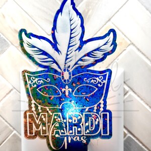 May include: A blue and gold Mardi Gras themed nightlight plug-in with a mask and feathers. The text "Mardi Gras" is on the bottom of the nightlight.