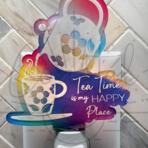Puede incluir: Una luz nocturna colorida con enchufe con un diseño de tetera y taza de té. El texto dice "Tea Time is my Happy Place".