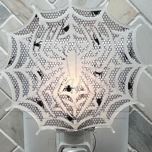May include: White plastic night light with a spiderweb design and black spiders. The night light has an on/off switch.