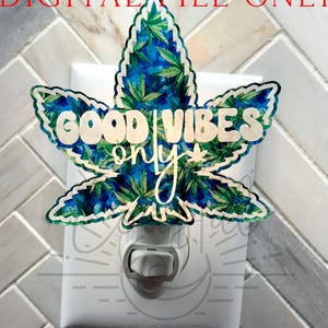 May include: A white night light plug-in with a green and blue marijuana leaf design. The leaf has the words "Good Vibes Only" written on it.