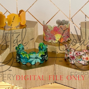 May include: Five different fabric bracelets displayed on wooden hexagonal stands. The bracelets are all different colors and patterns, including floral, geometric, and abstract designs. The bracelets are all made of fabric and have a scalloped edge.