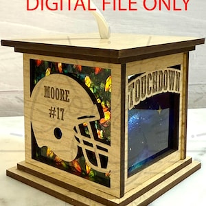 以下が含まれることがあります： 「DIGITAL FILE ONLY」の文字が入った、木製のフットボールをテーマにしたランタン。ランタンには、名前「MOORE」と番号「17」が入ったフットボールヘルメットの切り抜きがあります。「TOUCHDOWN」の文字も見えます。