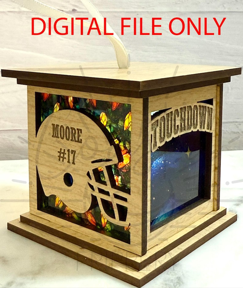以下が含まれることがあります： 「DIGITAL FILE ONLY」の文字が入った、木製のフットボールをテーマにしたランタン。ランタンには、名前「MOORE」と番号「17」が入ったフットボールヘルメットの切り抜きがあります。「TOUCHDOWN」の文字も見えます。