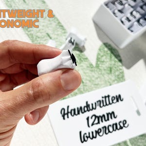 May include: A close-up of a white keycap held in a hand, with a black letter on it. The text "LIGHTWEIGHT & ERGONOMIC" is in orange letters. A tag reads "Handwritten 12mm lowercase".