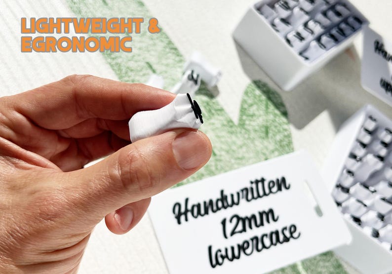 May include: A close-up of a white keycap held in a hand, with a black letter on it. The text "LIGHTWEIGHT & ERGONOMIC" is in orange letters. A tag reads "Handwritten 12mm lowercase".