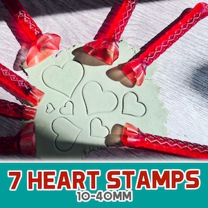 Puede incluir: Siete sellos rojos en forma de corazón de diferentes tamaños, que van de 10 a 40 milímetros, se muestran sobre una superficie verde claro. Los sellos están hechos de plástico rojo transparente y tienen un diseño texturizado.
