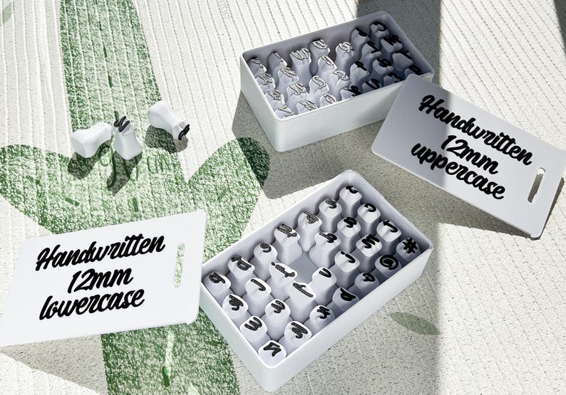 May include: White stamp sets with black lettering, including uppercase and lowercase options, are displayed. The text "Handwritten 12mm" is visible on the white labels. The stamps are in white boxes.