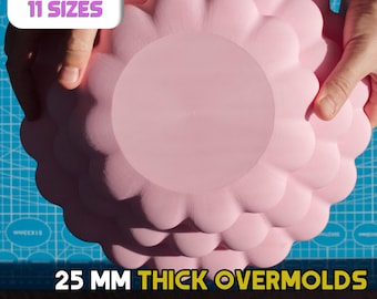 May include: Three pink ceramic molds for making plates. The molds are 25 mm thick and have a scalloped edge. The text "3 SHAPES 11 SIZES" and "25 MM THICK OVERMOLDS FOR CERAMIC PLATES" is visible in the image.