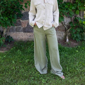 Op de afbeelding: Een vrouw draagt een lichtbeige linnen shirt en een wijde, lichtgroene linnen broek.