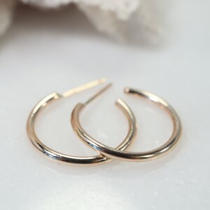 May include: A pair of small, gold-colored hoop earrings. The earrings are circular with a simple, polished design. The posts are visible, indicating they are designed to be inserted through pierced ears. The earrings are displayed on a white surface.