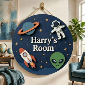 May include: A round, navy blue wooden sign with the text "Harry's Room" in white. The sign features a rocket, planet, astronaut, alien, and gold stars. A jute rope is attached for hanging.