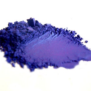 May include: A pile of loose purple pigment powder. The powder is a deep, rich purple color and has a slightly metallic sheen.