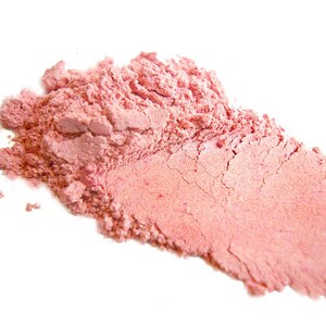Puede incluir: Primer plano de un rubor en polvo rosa. El polvo es finamente molido y tiene una textura suave y sedosa.