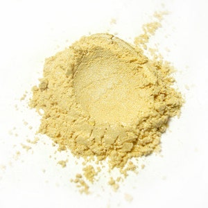 Puede incluir: Un pequeño montón de polvo de purpurina cosmética amarillo dorado sobre una superficie blanca.