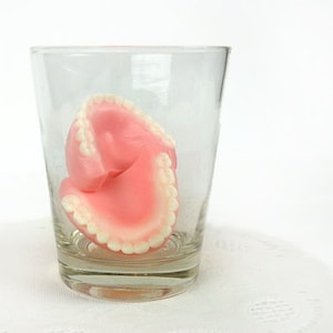 Pode incluir: Um conjunto de dentaduras postiças rosa e brancas em um copo transparente.