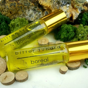 May include: Two small glass bottles with gold caps and yellow liquid inside. The bottles are labeled "bitter tundra boreal".