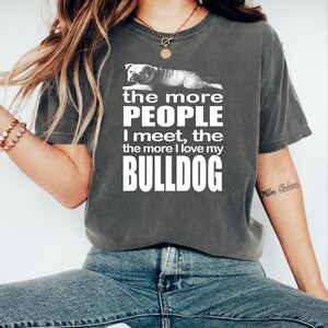 May include: Dark gray t-shirt with the text "the more PEOPLE I meet, the more I love my BULLDOG" in white. A graphic of a bulldog is above the text. The shirt is a comfortable, casual style.