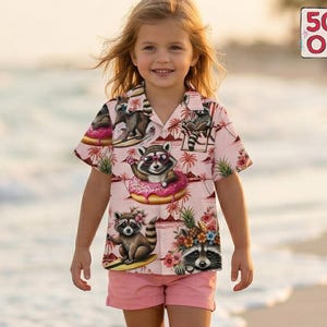 May include: A young girl wearing a pink button-down shirt and matching shorts walks on a beach. The shirt features a repeating pattern of raccoons on surfboards, donuts, and floral arrangements. A 50% off sign is visible in the upper right corner.