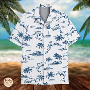 Könnte beinhalten: Weißes Hemd mit Knöpfen und einem Muster aus blauen Delfinen und Palmen. Das kurzärmelige Hemd hat einen klassischen Kragen und eine lockere Passform, perfekt für einen lässigen Look am Strand. Das Design umfasst verschiedene Delfinposen und tropische Insel-Elemente.