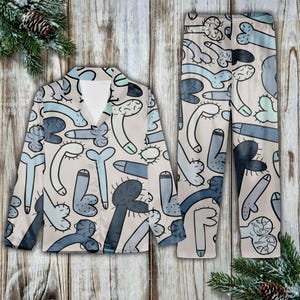 May include: A pajama set featuring a button-down shirt and matching pants. The set is beige with a repeating pattern of stylized blue and gray phallic shapes. The shirt has a V-neck and long sleeves. The pants are straight-legged.