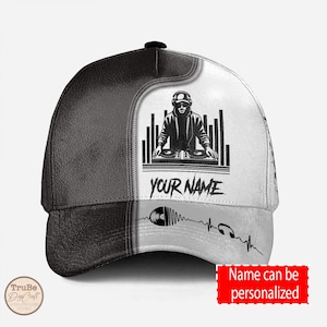 May include: Black and white baseball cap with a DJ graphic and the text "YOUR NAME". The cap has a black leather bill and a white mesh back.
