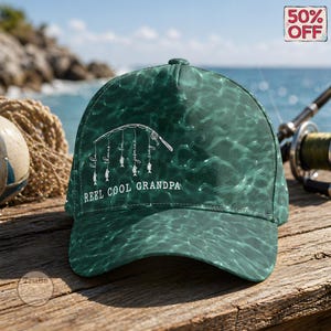 Op de afbeelding: Groene baseballpet met een waterachtig patroon. De pet heeft een hengelontwerp met de woorden "Reel Cool Grandpa" en namen. Een "50% OFF" sticker is zichtbaar.