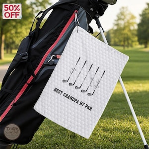 May include: White golf towel with a honeycomb pattern, displaying black golf club illustrations and the text "BEST GRANDPA BY PAR." The towel is hanging on a golf bag, with a "50% OFF" sticker visible.