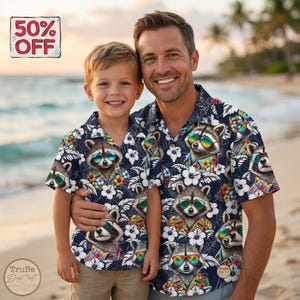 May include: Matching navy blue short-sleeve shirts featuring a raccoon wearing sunglasses and a floral shirt. The shirts have a white floral pattern. A father and son are wearing the shirts on a beach.