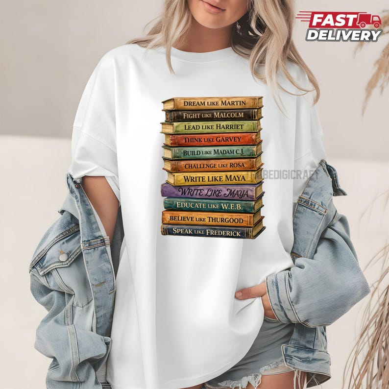 May include: White t-shirt featuring a stack of books with inspirational phrases like "Dream Like Martin" and "Write Like Maya." The books are in various colors, with gold lettering. The shirt has a relaxed fit.