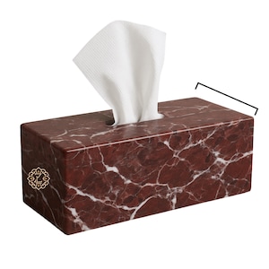 May include: A rectangular tissue box made of red marble with white veining. White tissues are pulled from the top opening. A gold emblem is on the lower left corner. The tissue box measures approximately 9 inches long.