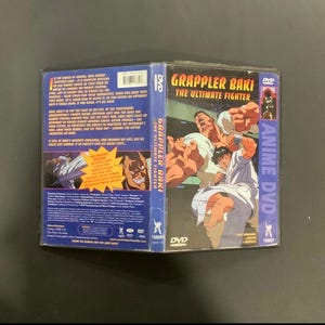 Puede incluir: Una caja de DVD para el anime "Grappler Baki: The Ultimate Fighter". La portada presenta ilustraciones de hombres musculosos en poses de lucha. La columna vertebral dice "Anime DVD" en p&uacute;rpura. La parte posterior de la caja tiene texto e im&aacute;genes.