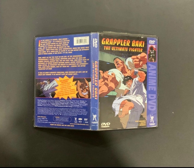 Puede incluir: Una caja de DVD para el anime "Grappler Baki: The Ultimate Fighter". La portada presenta ilustraciones de hombres musculosos en poses de lucha. La columna vertebral dice "Anime DVD" en p&uacute;rpura. La parte posterior de la caja tiene texto e im&aacute;genes.