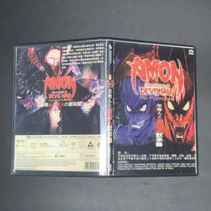 May include: DVD case for "Amon: Apocalypse of Devilman" featuring a demonic character illustration in red, blue, and purple. The title is in English and Japanese, with additional Japanese text. The case is open, showing the front and back covers.