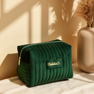a green velvet bag sitting on a bed next to a vase
