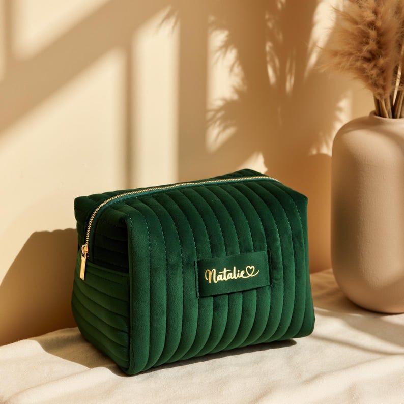a green velvet bag sitting on a bed next to a vase