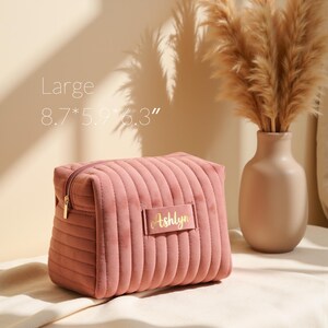 a pink purse sitting on top of a bed next to a vase