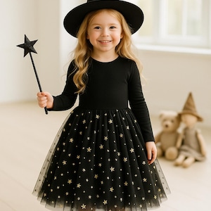 May include: A young child dressed in a black witch costume, including a long-sleeved top, a star-patterned skirt, and a pointed hat. The child holds a star-shaped wand. The outfit is suitable for Halloween or costume parties.