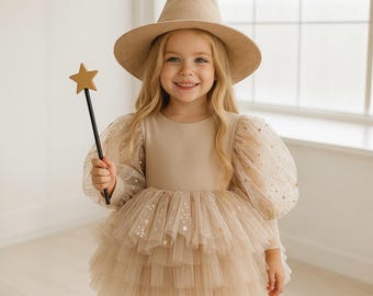 May include: A beige dress with long sheer puff sleeves and a multi-layered tulle skirt, both featuring gold star embellishments. The outfit includes a matching beige pointed hat and a black wand topped with a gold star, creating a cohesive look.