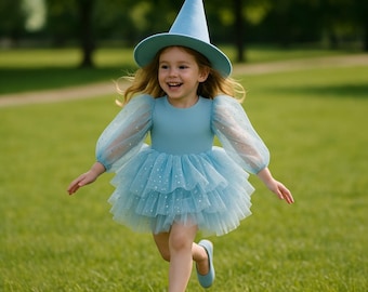 May include: A young child wearing a light blue witch costume, including a dress with a layered tulle skirt and a matching pointed hat. The dress has long, sheer sleeves. The child is running on green grass.