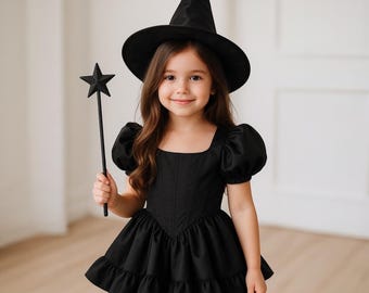 May include: A black witch costume consisting of a pointed hat, a dress with puff sleeves, a square neckline, and a ruffled skirt, accompanied by a black star-topped wand. The ensemble is entirely black, featuring a structured bodice design.