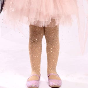 Puede incluir: Un atuendo infantil con medias de red marr&oacute;n claro adornadas con peque&ntilde;os adornos brillantes. El atuendo incluye una falda de tul rosa y zapatos Mary Jane rosas brillantes a juego. El fondo es de color claro.