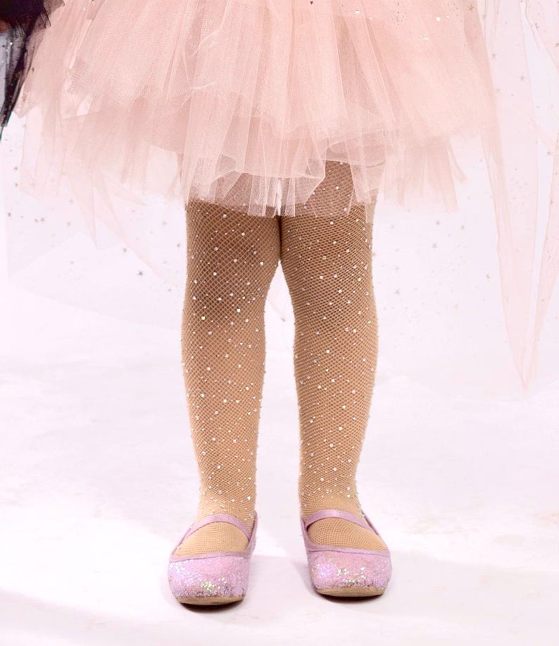 Puede incluir: Un atuendo infantil con medias de red marr&oacute;n claro adornadas con peque&ntilde;os adornos brillantes. El atuendo incluye una falda de tul rosa y zapatos Mary Jane rosas brillantes a juego. El fondo es de color claro.