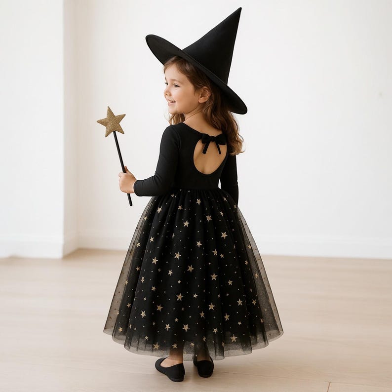 May include: A black witch costume for children, featuring a long-sleeved leotard with a star-patterned tulle skirt. The outfit includes a pointed witch hat and a star-shaped wand. The back of the leotard has a bow detail. The child is wearing black shoes.