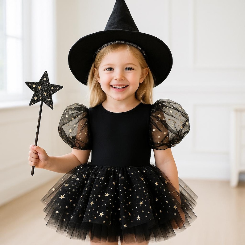 Puede incluir: Un ni&ntilde;o vestido con un disfraz de bruja negro, con un sombrero puntiagudo, una varita en forma de estrella y una falda tut&uacute; adornada con estrellas doradas. El disfraz tiene mangas transparentes con estampado de estrellas.